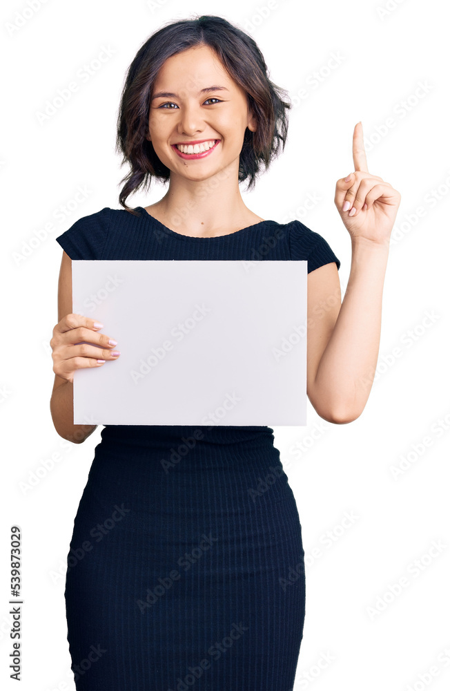 Young beautiful girl holding blank empty banner surprised with an idea or question pointing finger with happy face, number one Young beautiful girl holding blank empty banner surprised with an idea or question pointing finger with happy face, number one