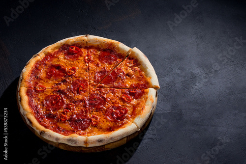 Pizza with tomato sauce, mozzarella, salami, chili, honey on black background. View from above
