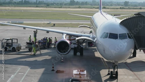 Unloading luggage in the airplane from passenger commercial plane and fueling with pipe attached to wing. Baggage and maintenance service in the airport, slow motion