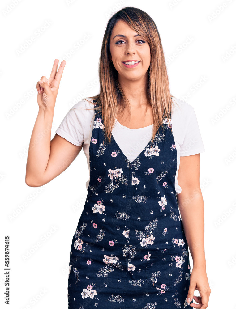 Young beautiful woman wearing casual floral dress smiling with happy face winking at the camera doing victory sign. number two. Young beautiful woman wearing casual floral dress smiling with happy face winking at the camera doing victory sign. number two.