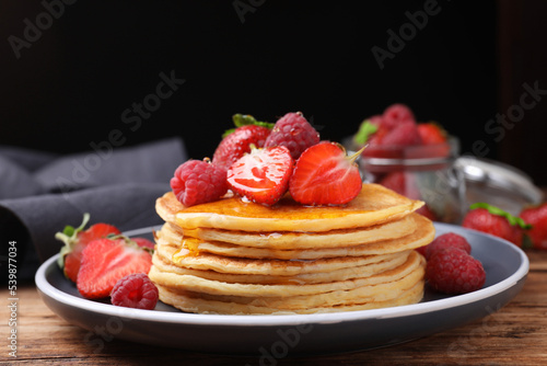 Tasty pancakes with fresh berries and honey on wooden table, closeup