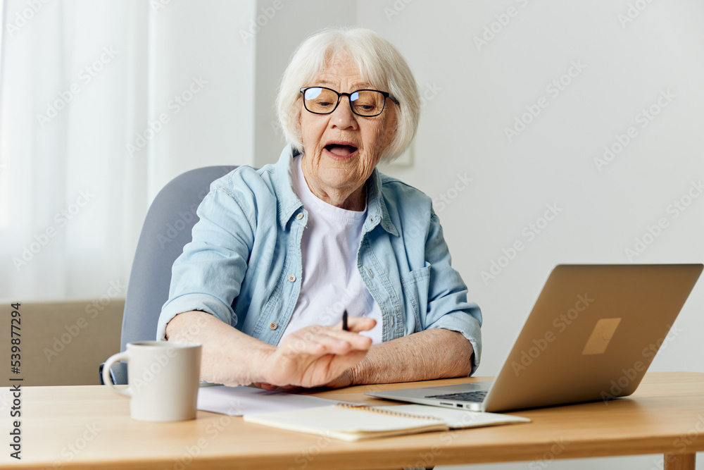 a business-like elderly lady works from home on a laptop at her desk and looks attentively while doing work a business-like elderly lady works from home on a laptop at her desk and looks attentively while doing work