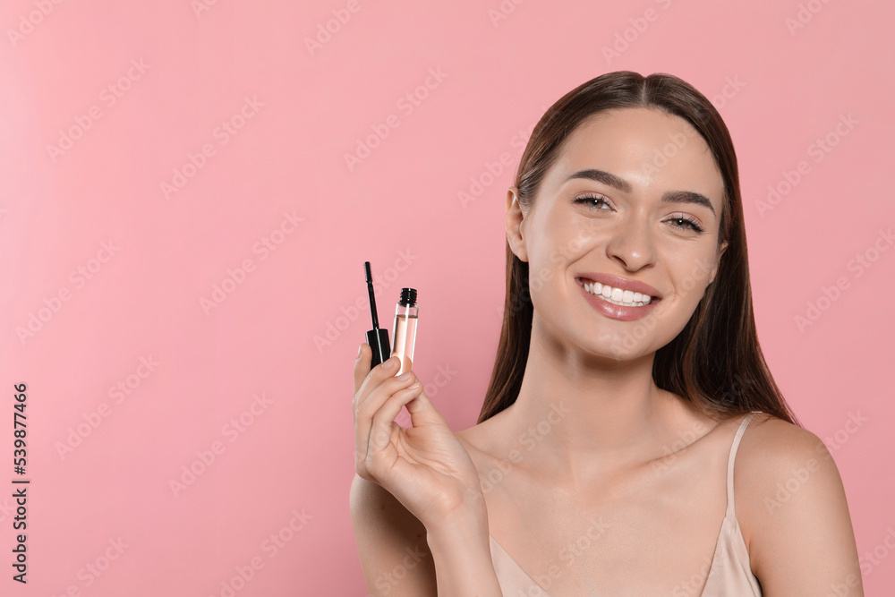 Fototapeta premium Young woman with eyelash oil on pink background, space for text