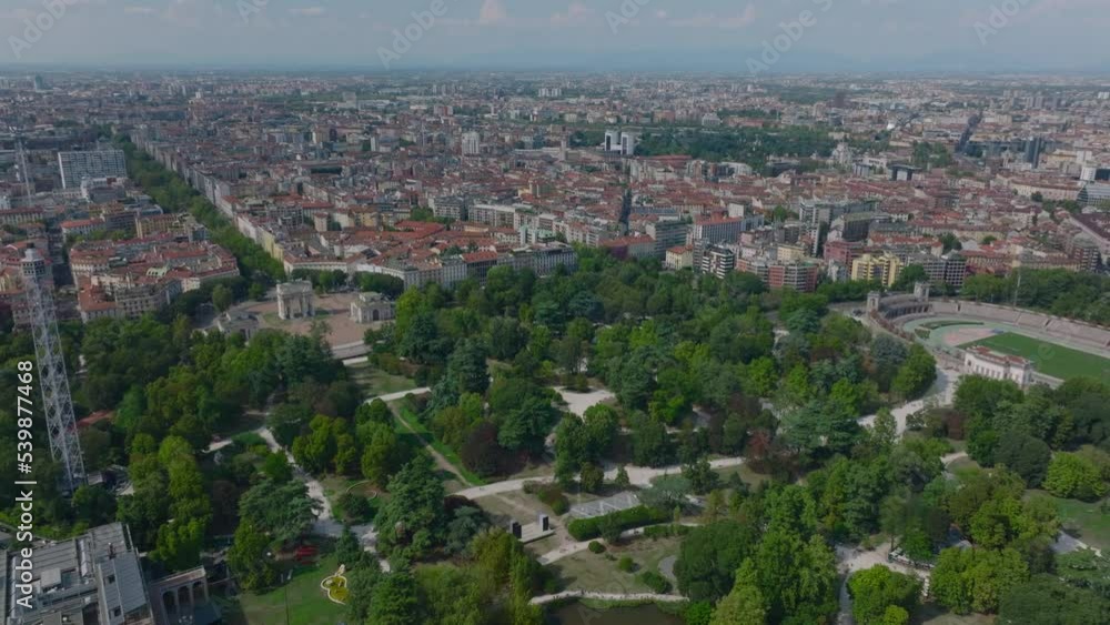 Forwards fly above green trees in Sempione Park. Panoramic view of buildings in urban boroughs. Milano, Italy Forwards fly above green trees in Sempione Park. Panoramic view of buildings in urban boroughs. Milano, Italy