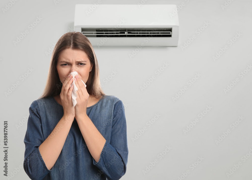 © New Africa - Woman suffering from cold in room with air conditioner on white wall, space for text © New Africa - Woman suffering from cold in room with air conditioner on white wall, space for text