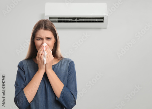 Leinwand Poster Woman suffering from cold in room with air conditioner on white wall, space for