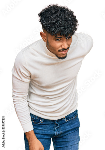 Young arab man wearing casual winter sweater suffering of backache, touching back with hand, muscular pain