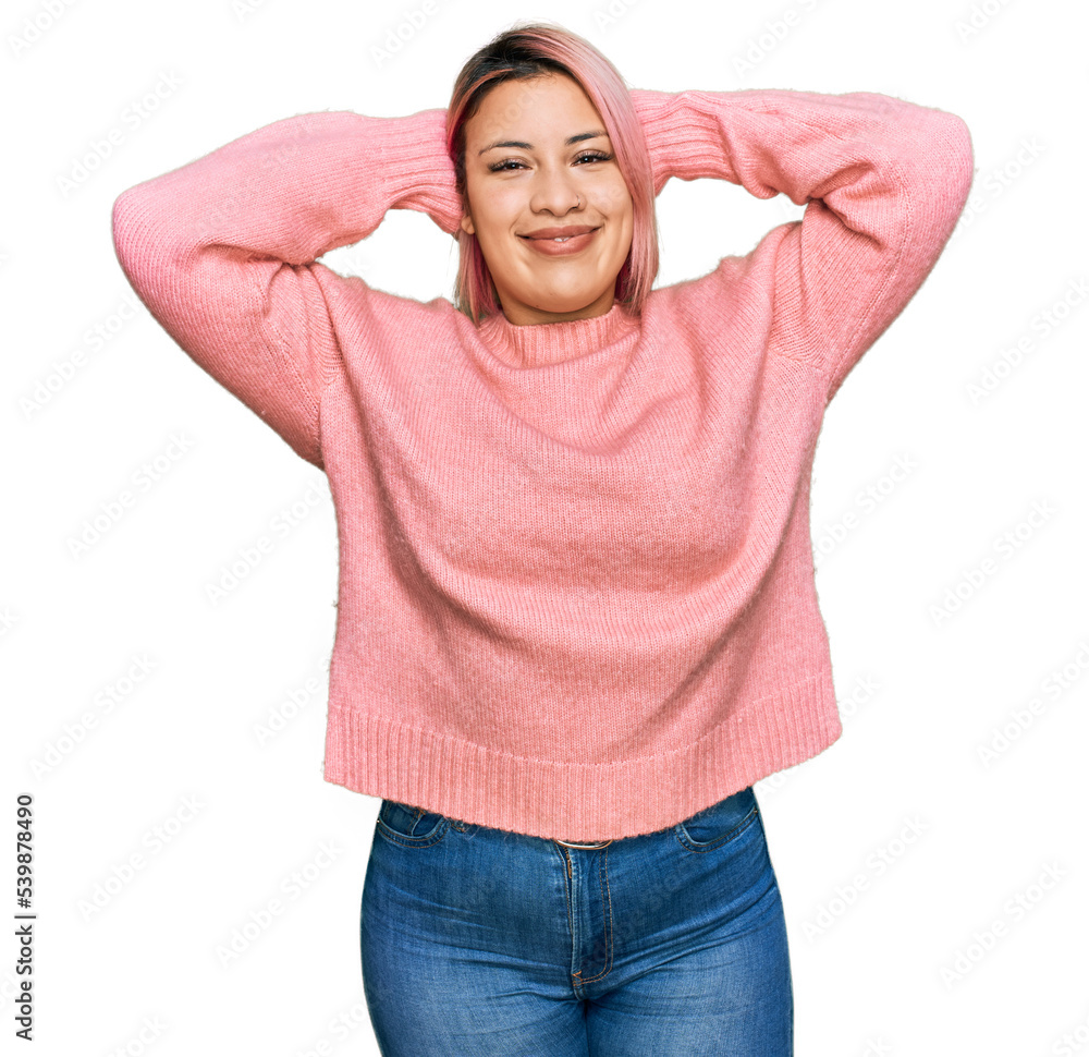 Hispanic woman with pink hair wearing casual winter sweater relaxing and stretching, arms and hands behind head and neck smiling happy Hispanic woman with pink hair wearing casual winter sweater relaxing and stretching, arms and hands behind head and neck smiling happy
