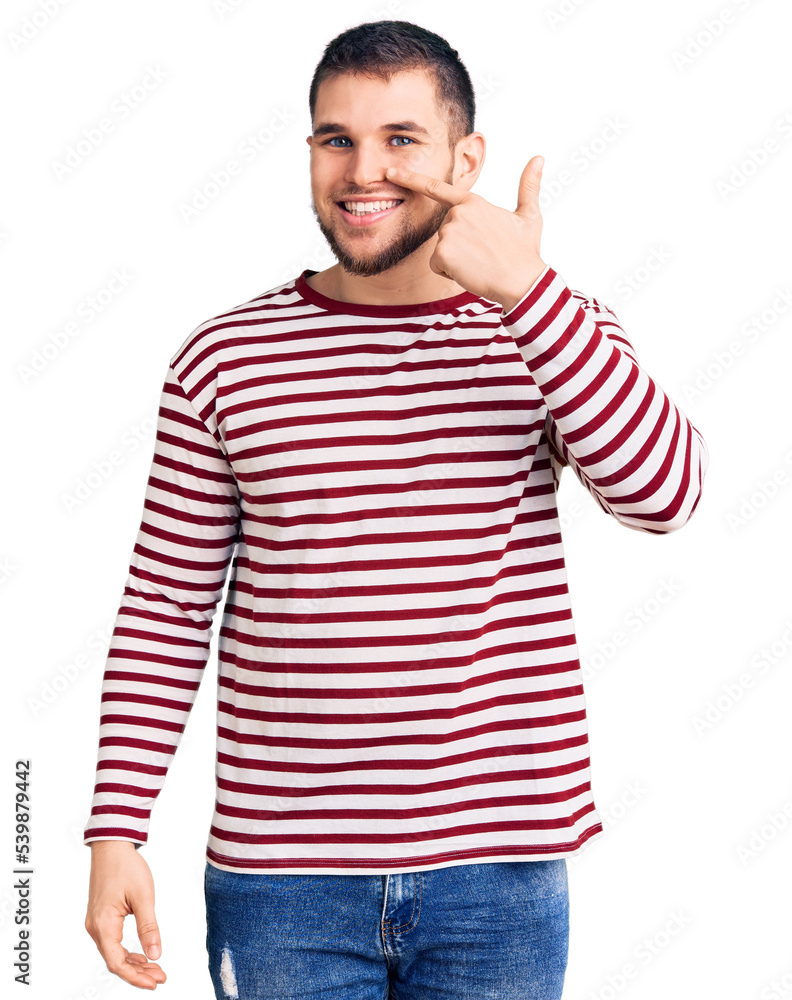 Young handsome man wearing striped sweater pointing with hand finger to face and nose, smiling cheerful. beauty concept Young handsome man wearing striped sweater pointing with hand finger to face and nose, smiling cheerful. beauty concept