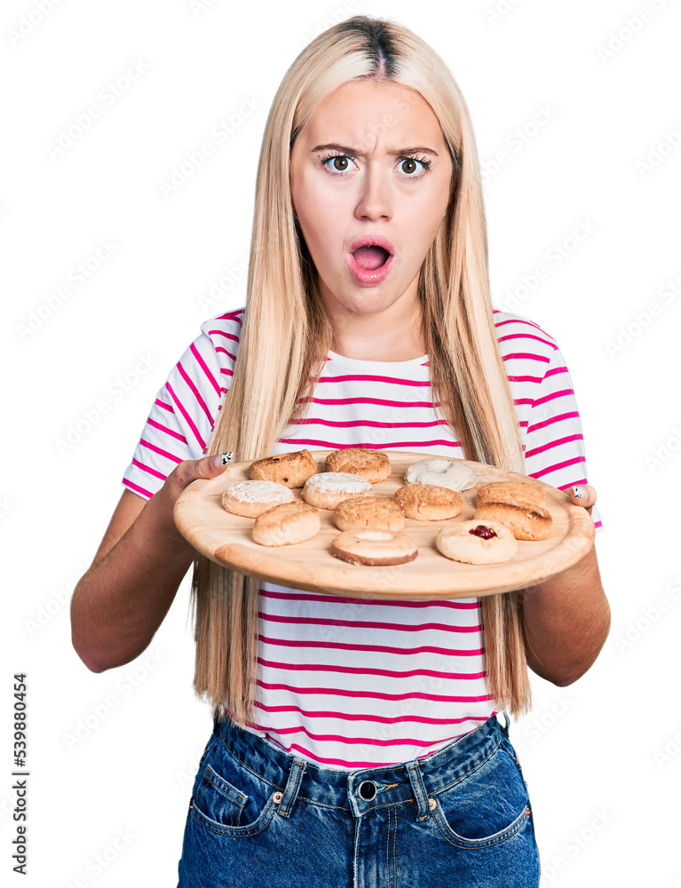 Beautiful blonde woman eating pastries afraid and shocked with surprise and amazed expression, fear and excited face. Beautiful blonde woman eating pastries afraid and shocked with surprise and amazed expression, fear and excited face.