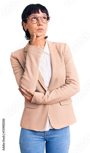 Young brunette woman with short hair wearing business jacket and glasses with hand on chin thinking about question, pensive expression. smiling with thoughtful face. doubt concept.