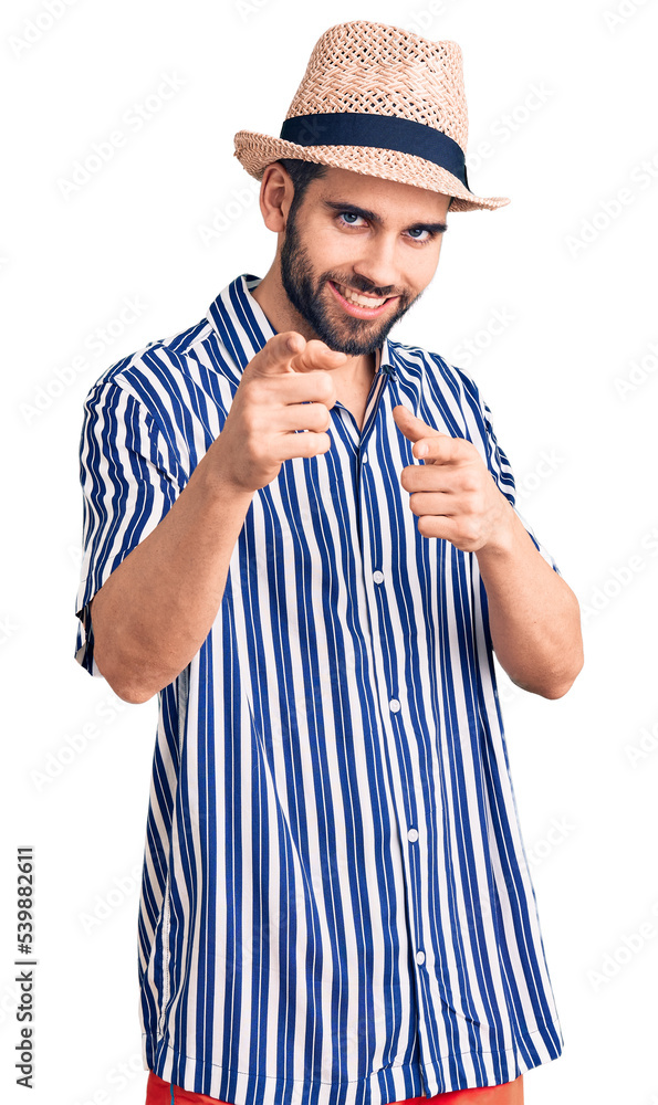 Young handsome man with beard wearing summer hat and striped shirt pointing fingers to camera with happy and funny face. good energy and vibes. Young handsome man with beard wearing summer hat and striped shirt pointing fingers to camera with happy and funny face. good energy and vibes.
