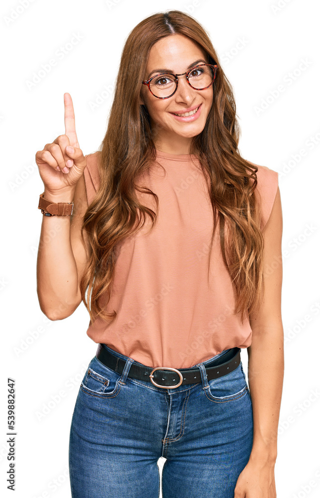 Young hispanic woman wearing casual clothes and glasses showing and pointing up with finger number one while smiling confident and happy. Young hispanic woman wearing casual clothes and glasses showing and pointing up with finger number one while smiling confident and happy.