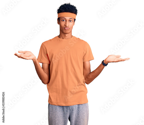 Young african american man wearing sportswear clueless and confused expression with arms and hands raised. doubt concept.