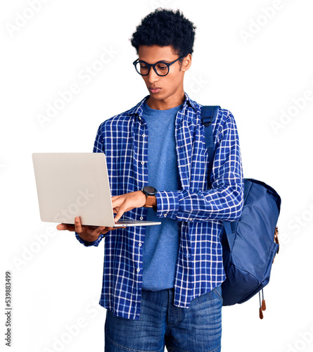 Young african american man holding student backpack using laptop thinking attitude and sober expression looking self confident