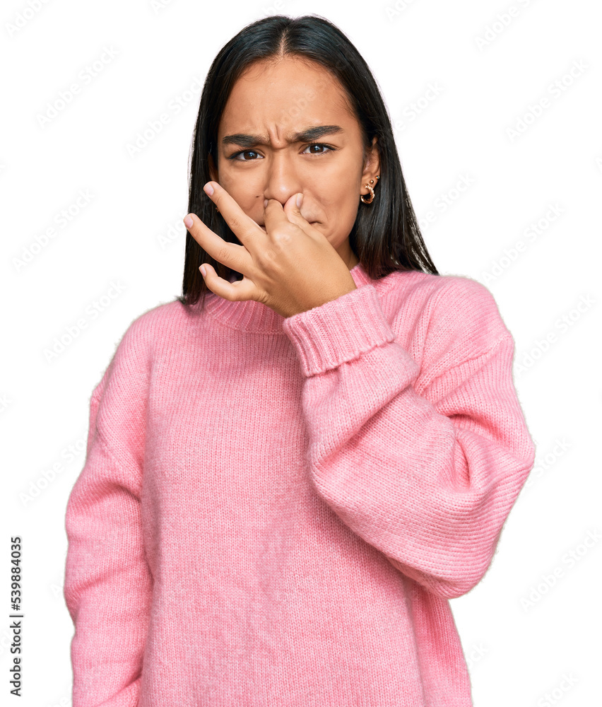 Young asian woman wearing casual winter sweater smelling something stinky and disgusting, intolerable smell, holding breath with fingers on nose. bad smell Young asian woman wearing casual winter sweater smelling something stinky and disgusting, intolerable smell, holding breath with fingers on nose. bad smell