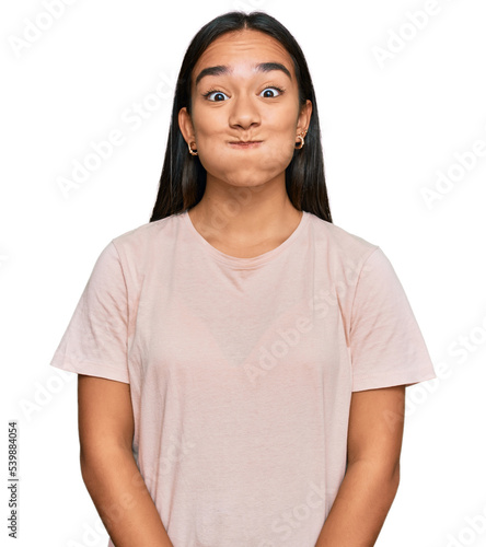 Young asian woman wearing casual clothes puffing cheeks with funny face. mouth inflated with air, crazy expression.