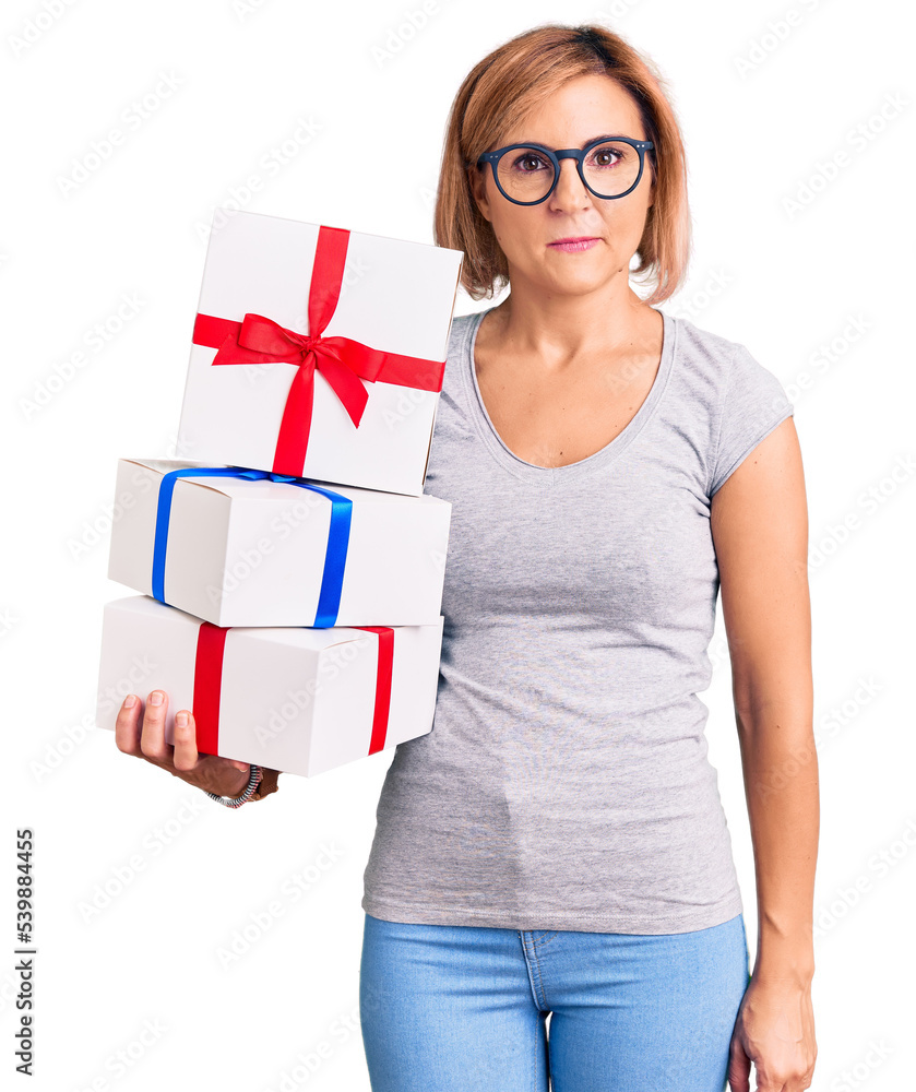 Young blonde woman wearing glasses holding gift thinking attitude and sober expression looking self confident Young blonde woman wearing glasses holding gift thinking attitude and sober expression looking self confident
