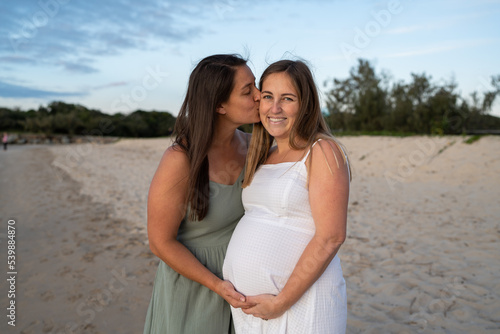 lesbian couple kissing on cheek at the beach