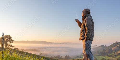 Fotografie Hiker Male with cup of coffee tea enjoying morning sunrise mist on mountain