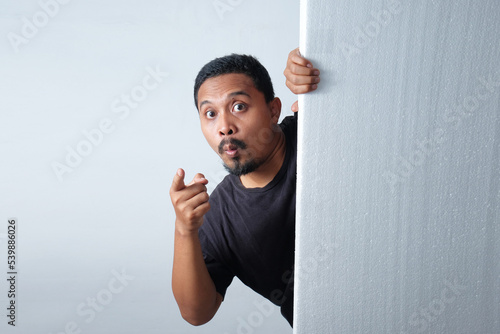 man peeking behind wall while pointing finger
