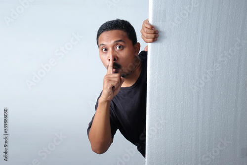 man peeking behind wall with silent gesture photo