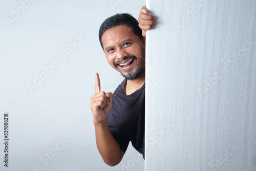 happy man peeking behind the wall while pointing finger up