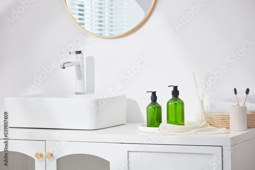 A light-colored sink has a mirror above and a faucet next to the hair care bottle, wooden towel tray, and toothbrushes. 