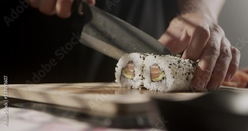 A chef cuts a sushi roll and prepares sushi. Detail on hand.