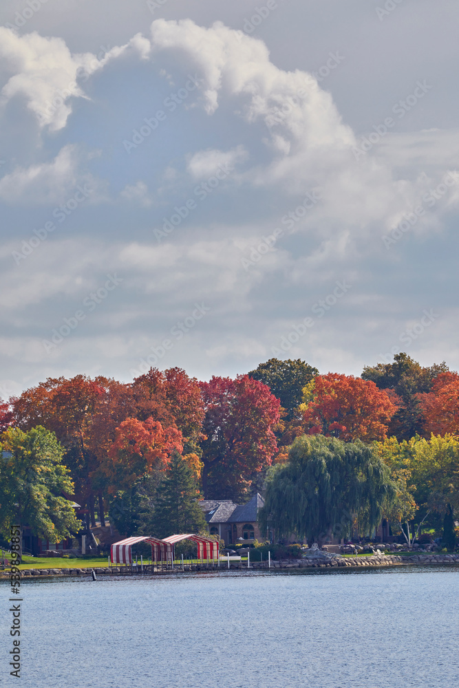 Fototapeta premium Fall trees turning vivid color on a river shoreline with big fluffy clouds in a bright blue sky