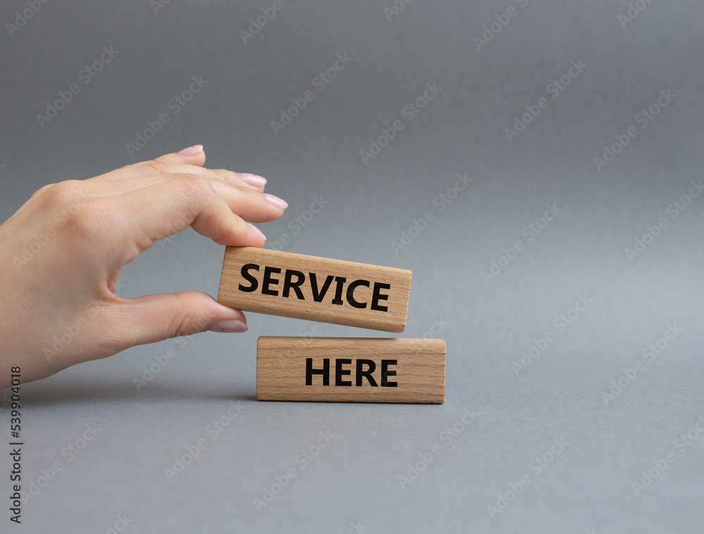 Service here symbol. Concept words Service here on wooden blocks. Beautiful grey background. Businessman hand. Business and Service here concept. Copy space.