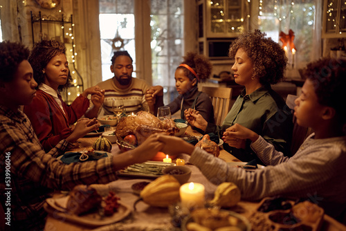 African American extended family saying grace while having Thanksgiving meal at dining table. photo