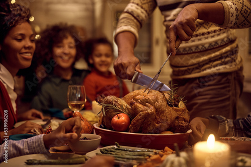Close up of black father carving Thanksgiving turkey during family lunch at dining table
