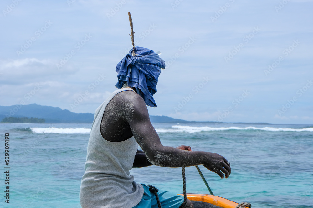 A Melanesian man sitting on the bow of a fishing boat wearing head