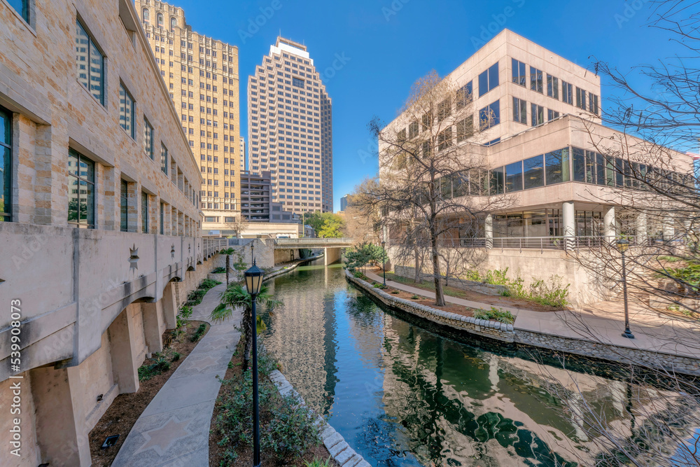 River Walk in San Antonio Texas along tall buildigs with blue sky background