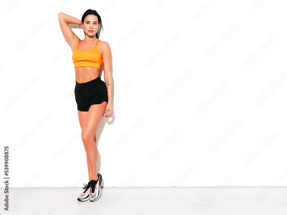 Portrait of fitness confident woman in black sports clothing. Sexy young beautiful model with perfect body. Female isolated on white wall in studio. Stretching out before training Portrait of fitness confident woman in black sports clothing. Sexy young beautiful model with perfect body. Female isolated on white wall in studio. Stretching out before training