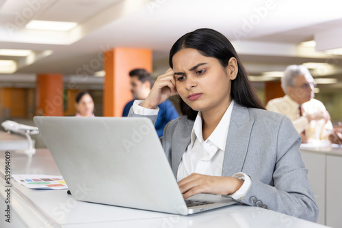 Thoughtful millennial professional solving problems using laptop in office.