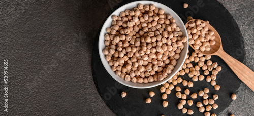 Bowl with raw chickpea and spoon on dark background with space for text