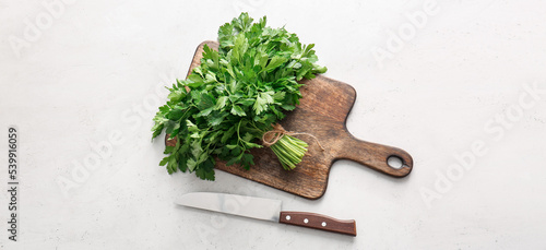 Cutting board with fresh parsley and knife on light background, top view