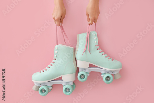 Woman holding vintage roller skates on color background photo