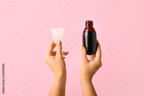 Woman with bottle of cough syrup and cup on pink background photo