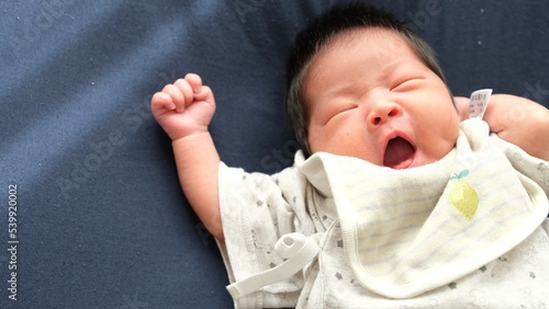 産後1か月0歳の新生児が右手を上にあくびしている右寄りの写真 photo