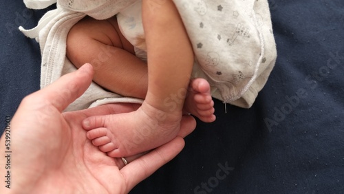 産後1か月の0歳児の新生児の足に大人が手を添えている写真 photo