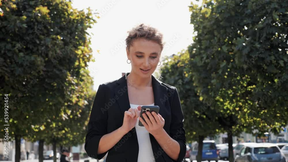 Happy beautiful blond woman manager CEO in formal outfit smiling, holding smartphone in hands typing message browsing internet, successful lady completing her work in time, freedom and positivity. Happy beautiful blond woman manager CEO in formal outfit smiling, holding smartphone in hands typing message browsing internet, successful lady completing her work in time, freedom and positivity.