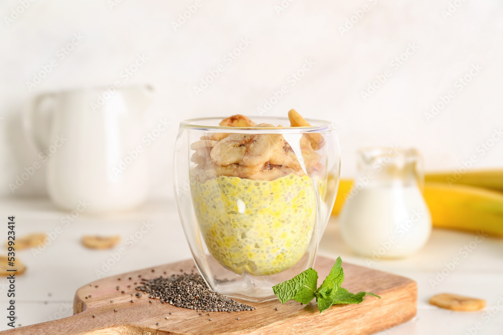 Wooden board with glass of tasty chia seed pudding and banana on light table