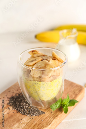 Wooden board with glass of tasty chia seed pudding and banana on light table