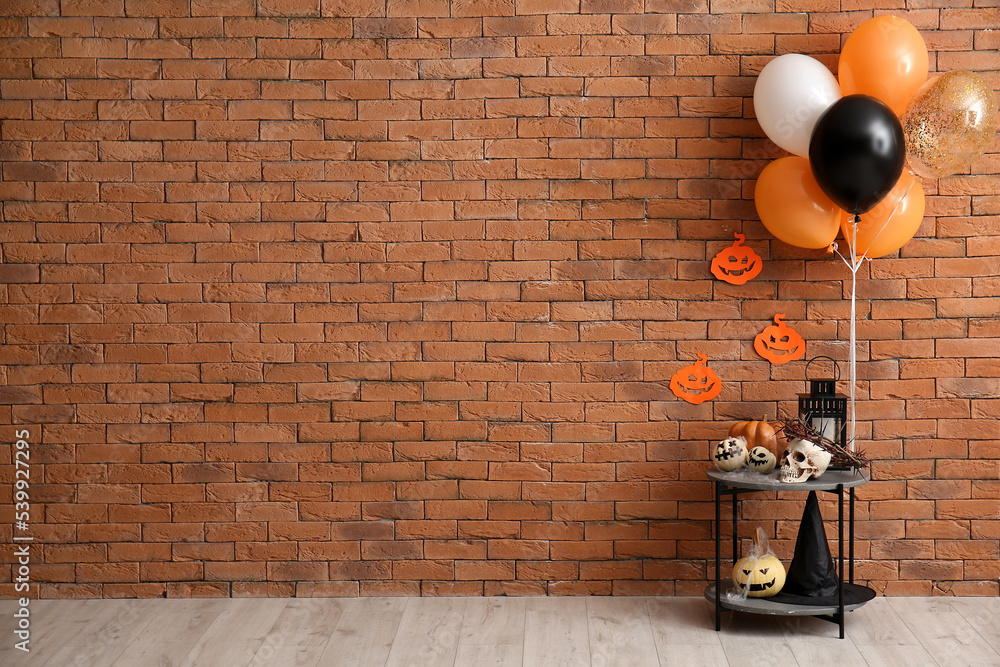 Table with Halloween pumpkins, skull and balloons near brick wall