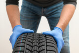 Closeup of mechanic hands pushing a black tire on a white background. Replacement of winter and summer tires. Cropped Hands Of Mechanic.