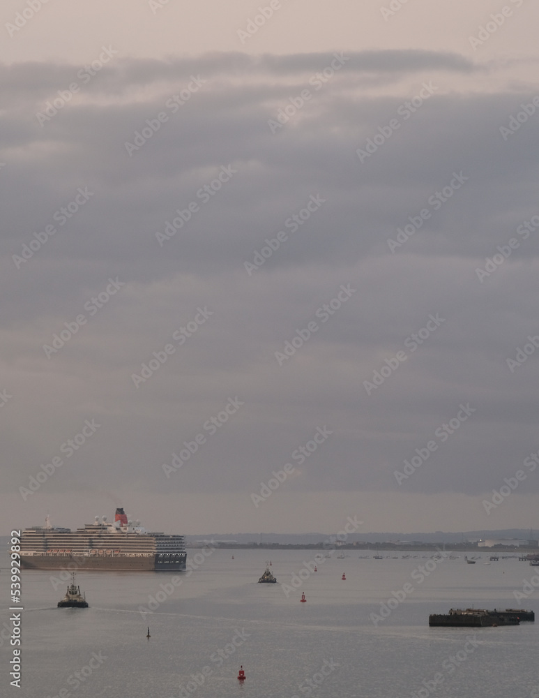 Luxury Cunard ocean cruiseship cruise ship liner Queen Victoria arrival into port of Southampton, England during early morning dusk twilight hour