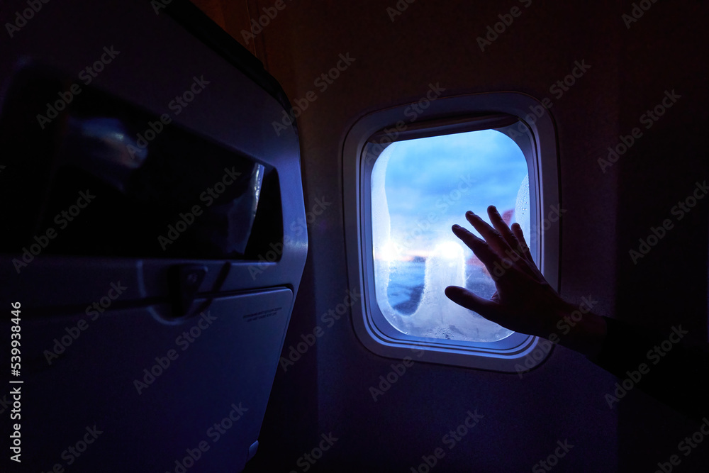 Female hand touches the warm sun rays from airplane window. Woman looking forward to travel on her vacation. Girl on a journey flight sitting in aircraft and enjoys sun flares. Female hand touches the warm sun rays from airplane window. Woman looking forward to travel on her vacation. Girl on a journey flight sitting in aircraft and enjoys sun flares.